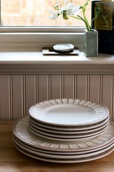 a stack of white plates sitting on top of a wooden table next to a window