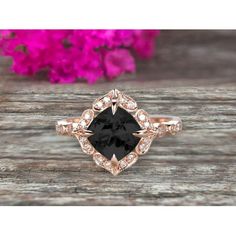 a black and white diamond ring on top of a wooden table with pink flowers in the background