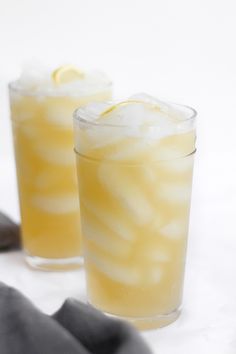 two glasses filled with lemonade sitting on top of a white table next to a gray napkin