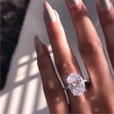 a woman's hand with a ring on top of her finger and an oval shaped diamond in the middle