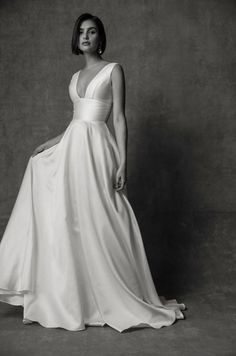 a woman in a long white dress posing for a black and white photo with her hands on her hips