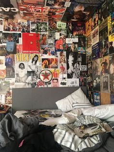 an unmade bed in front of a wall covered with posters