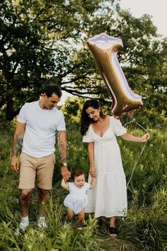 a man, woman and baby are standing in the grass with a large number balloon