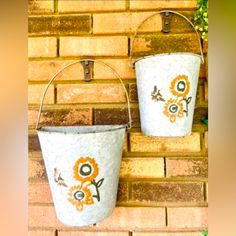 two buckets with flowers painted on them are hanging from a brick wall in front of a planter