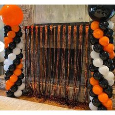 an orange, black and white balloon arch in front of a fireplace