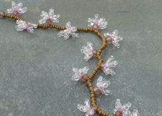 a beaded necklace with flowers and beads on a stone surface in front of a brick wall