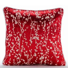 a red pillow with white flowers and branches printed on it, sitting on a white surface