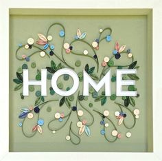 the word home is made out of buttons and leaves in a frame with white trim