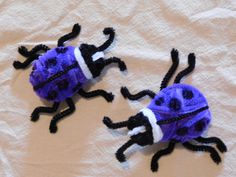 two purple and black bugs are on a white sheet, one is made out of yarn