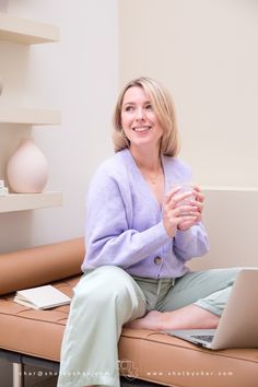 a woman sitting on a couch with a laptop in her lap and smiling at the camera