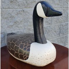 a black and white duck sitting on top of a wooden table next to a brick wall