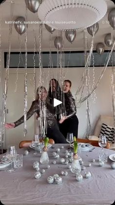 two women standing in front of a table with silver balloons hanging from it's ceiling