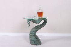 a glass table with a bottle on it and a mermaid tail shaped stand next to it