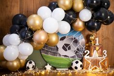 a table topped with balloons and soccer balls next to a wooden wall covered in gold, white and black decorations