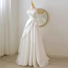 a white wedding dress is on display in front of a mirror with a gold bow