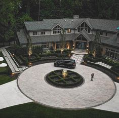 a car is parked in front of a large house with a circular driveway and landscaping