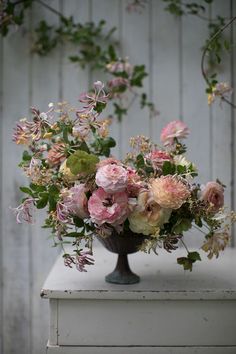 a vase filled with lots of pink flowers on top of a white table next to a wooden wall