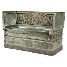 a green velvet couch with fringe trimmings and an ornate design on the back