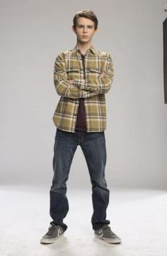 a young man standing in front of a tv set with his arms crossed and looking at the camera