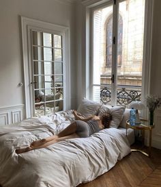 a woman laying on top of a bed in a bedroom next to a large window