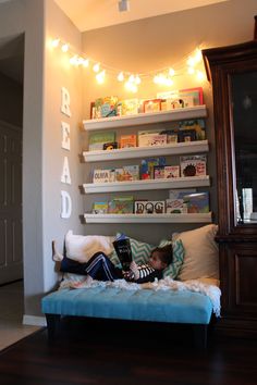 a kid laying on top of a bed in a room next to a book shelf