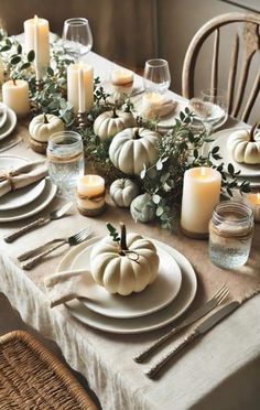 a table set with white pumpkins, candles and greenery