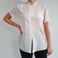 Gorgeous, cheongsam style blouse in white with a beautiful floral embroidery across the front and collar. It has a straight shape, mandarin collar, short sleeves, six buttons and side slits. The blouse is made from a lightweight fabric. A perfect, smart blouse for any occasions. Made by St Michael. 100% polyester. No size label, would fit Medium size. Measurements when laid flat are: Pit to pit: 54cm Waist: 51cm Length: 68cm. Excellent condition, as new. B. Fitted Stand Collar Blouse For Summer, Fitted Summer Blouse With Stand Collar, White Stand Collar Blouse With Buttons, White Blouse With Stand Collar And Buttons, White Stand Collar Tops For Daywear, White Short Sleeve Formal Blouse, Formal White Short Sleeve Blouse, Formal Embroidered Short Sleeve Blouse, Traditional Short Sleeve White Blouse