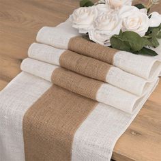 a stack of towels sitting on top of a wooden table next to white flowers and greenery