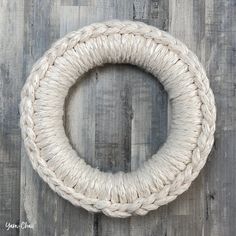 a white rope wreath on top of a wooden floor next to a gray wood wall