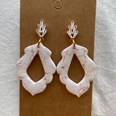 pair of earrings with white marble and gold accents on brown carding paper, closeup