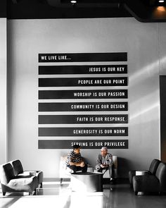 two people sitting on couches in front of a wall with words written on it