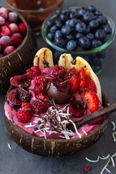 fruit and chocolate in coconut bowls with spoons on the table next to other fruits