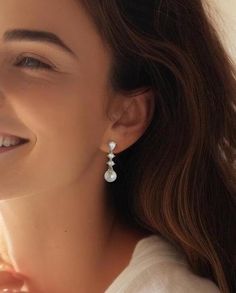 a woman wearing earrings with pearls on the bottom and one bead hanging from it