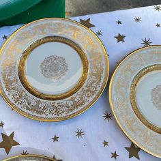 two gold and white plates sitting on top of a tablecloth with stars around them