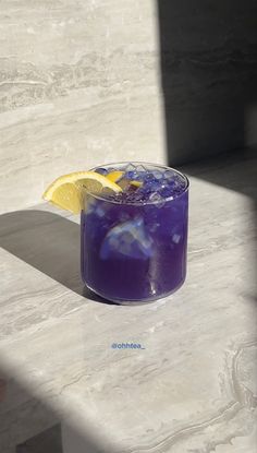 a purple drink sitting on top of a table next to a slice of lemon wedge