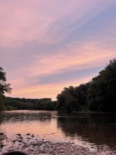 the sun is setting over a river with rocks and trees in it, as seen from the shore