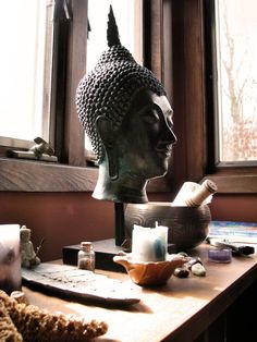 a buddha head sitting on top of a wooden table next to a bowl and candle