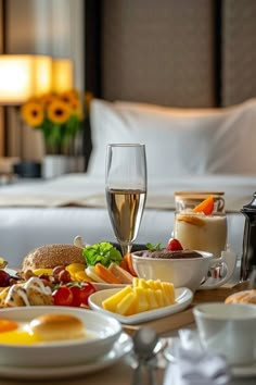 a table filled with food and drinks on top of a wooden table next to a bed