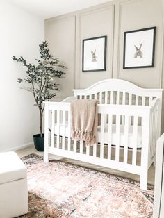 a white crib in a room with two pictures on the wall and a potted plant