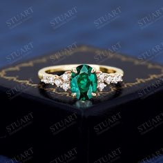 an emerald and diamond ring sitting on top of a black box with gold trimming