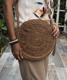 a woman is holding a brown purse on her shoulder and standing in front of some plants