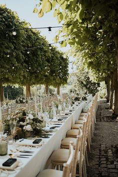 a long table is set with white linens and place settings for an outdoor dinner