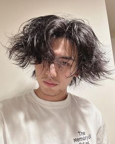 a man with long hair standing in front of a white wall wearing a t - shirt