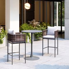 two wicker chairs and a round table on the ground in front of a building