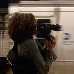 a woman with curly hair is holding a camera in front of a subway train as it passes by