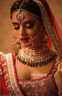 a woman in a red and gold bridal outfit with jewelry on her head, looking down