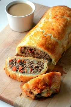 a meat and cheese roll cut in half on a cutting board with a cup of coffee