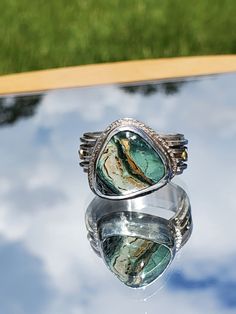 This ring features a 15 x 11mm Turquoise gemstone set in Sterling Silver and accented with two, 14kt gold balls.  The turquoise features bands of gold, cream, light green and dark green.  It is cut in a triangle shape and set at an angle to best compliment a woman's finger.  The band is 10 mm wide and features 4 individual bands of Sterling Silver to give it a multi-dimensional look.  The gold balls accent the gold in the turquoise. This is a one-of-a-kind ring that you will not see anywhere else. RETURN POLICY: I accept returns under the following conditions.  The jewelry must be returned in new condition.  Purchaser must contact me within 3 days of receipt of the jewelry.  The ring must be returned in the same jewelry box it was shipped in, and it must be returned vias USPS Priority Mail Green Turquoise Ring With Natural Stones, Unique Green Turquoise Ring With Large Stone, Unique Turquoise Chrysoprase Jewelry, Artisan Green Jewelry With Large Stone, Green Chrysocolla Rings With Natural Stones, Green Chrysocolla Cabochon Jewelry, Artisan Green Chrysocolla Rings, Green Chrysocolla Gemstone Ring, Green Chrysocolla Gemstone Jewelry