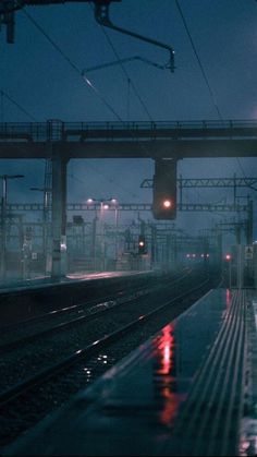 an empty train station at night with rain on the tracks and traffic lights in the background