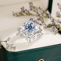 a blue diamond ring sitting on top of a green box next to some purple flowers